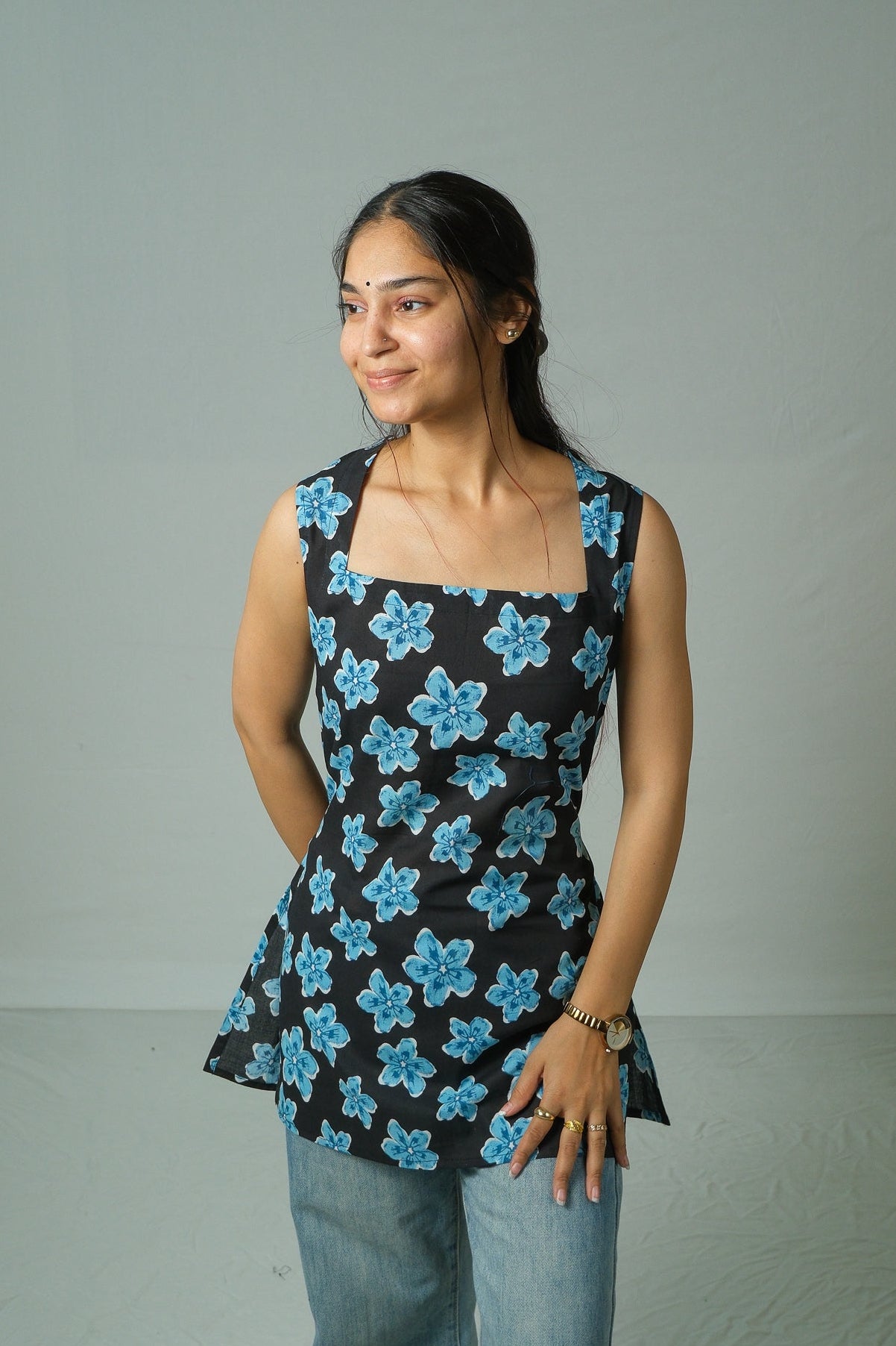 Woman wearing a black sleeveless top with blue floral patterns against a plain background