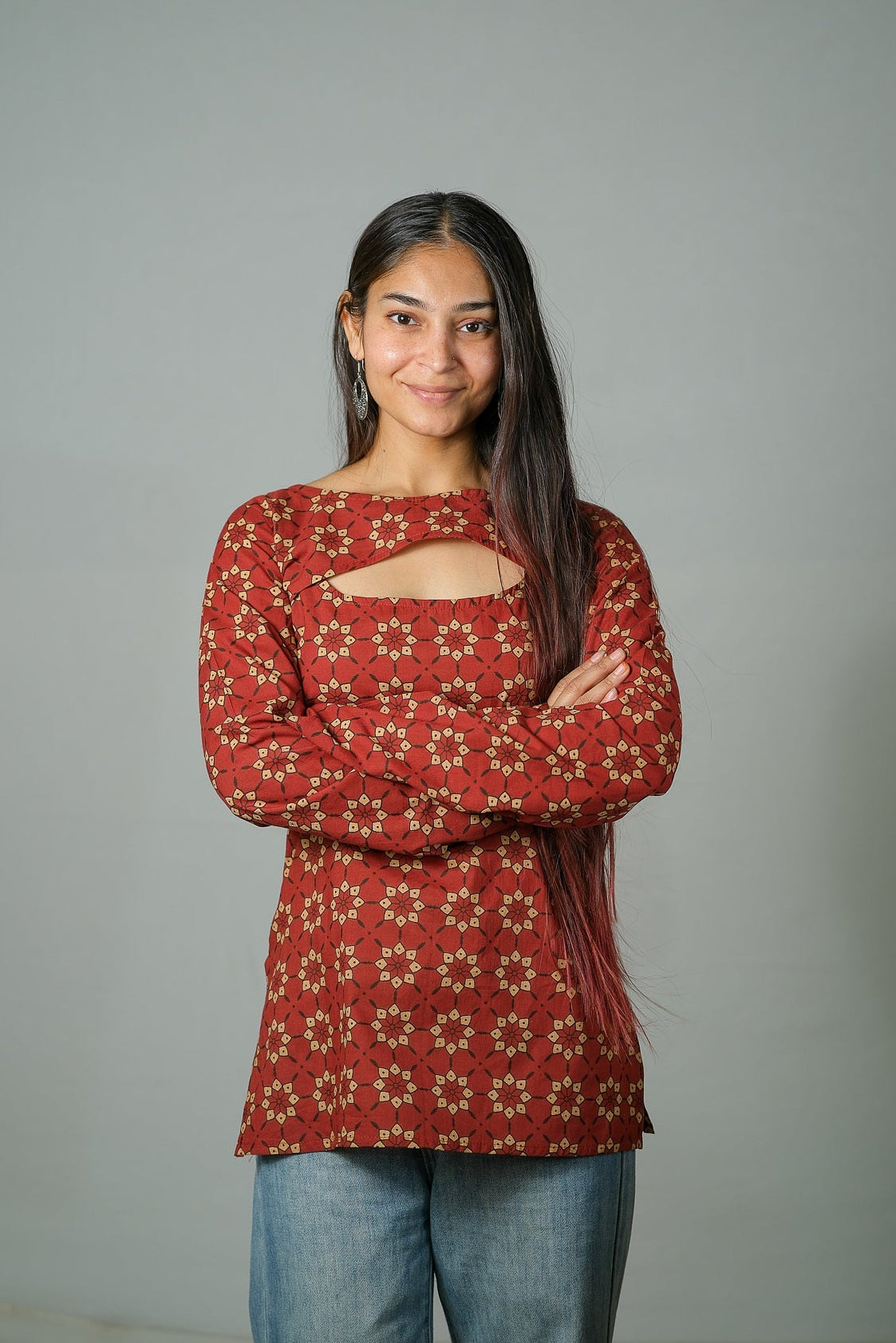 Woman wearing a red patterned top with cut-out design, standing against a plain background