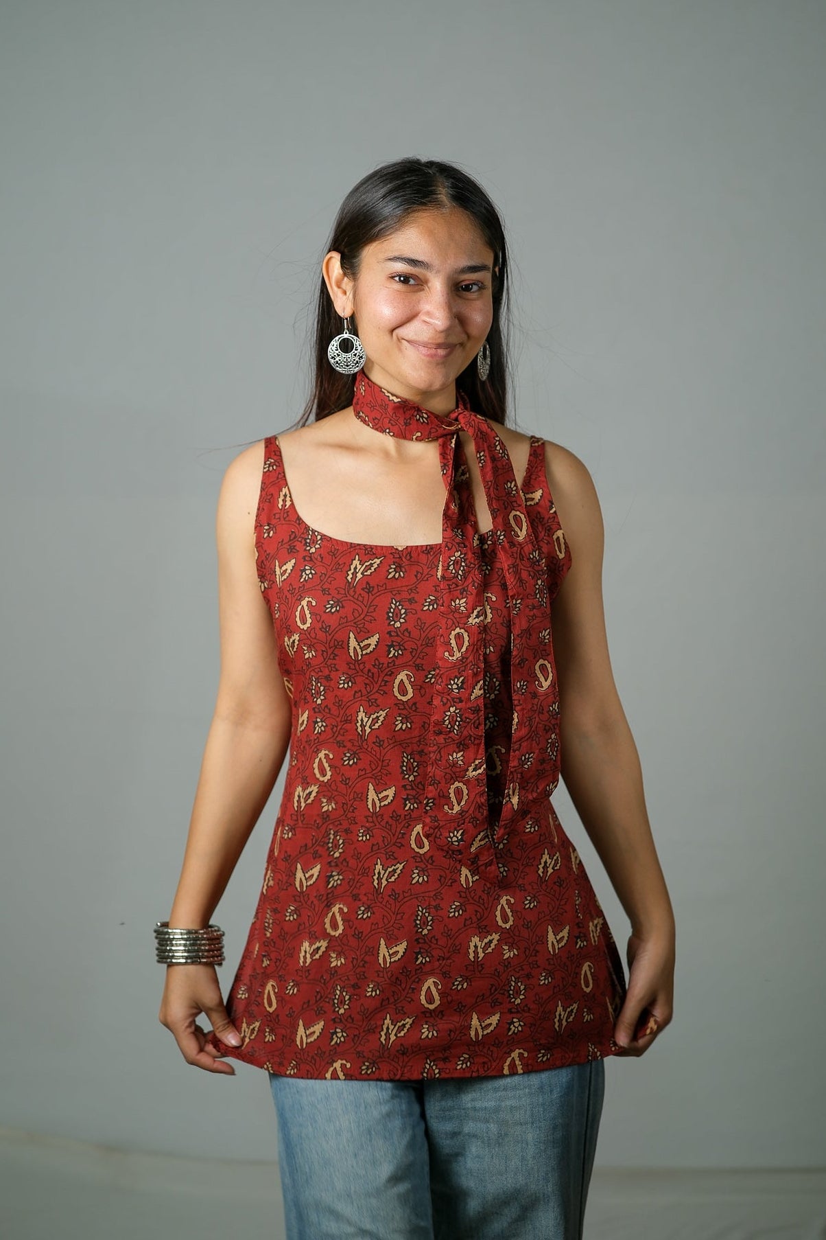 Woman wearing a red patterned top with a scarf, standing against a gray background