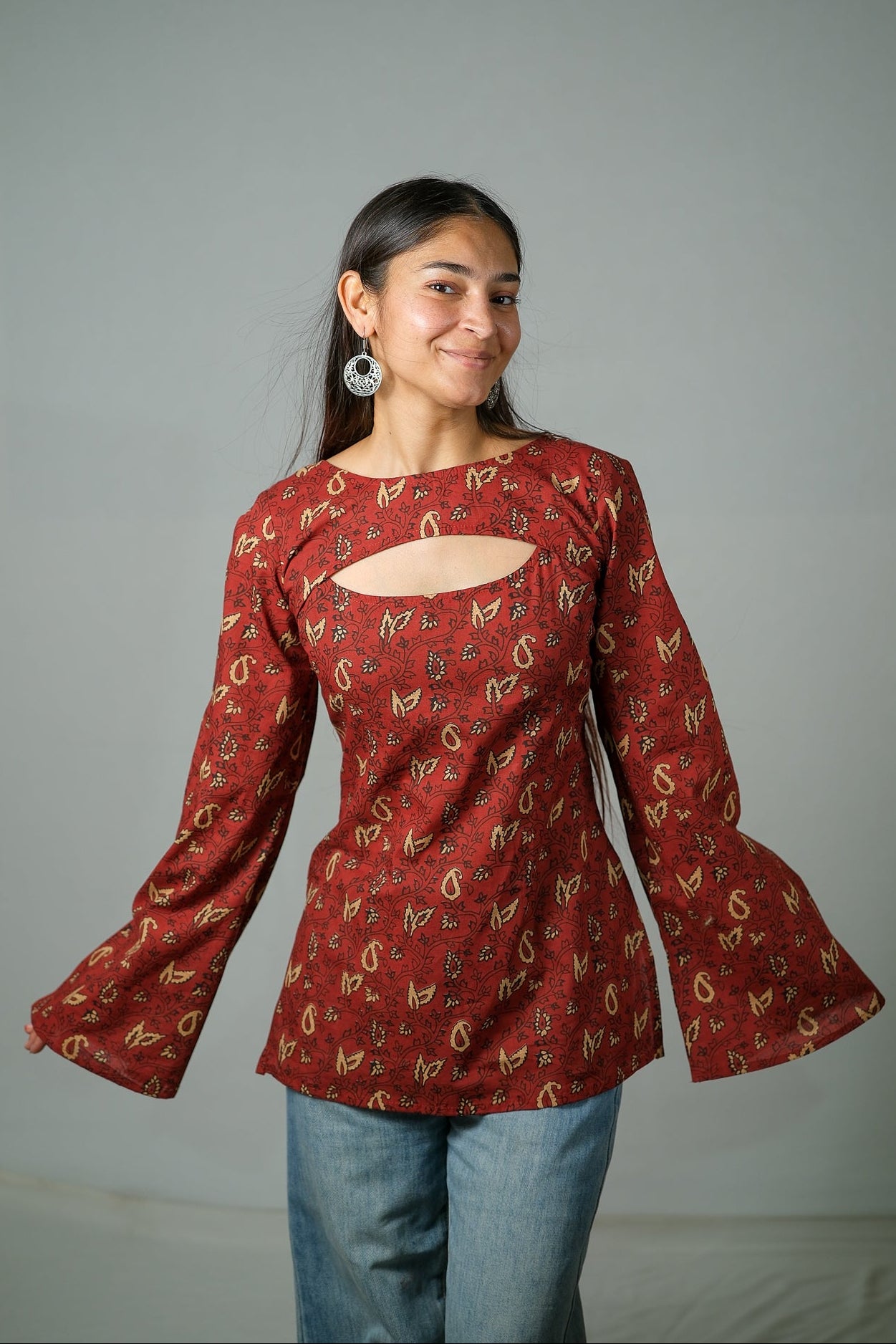 Woman wearing a red patterned kurti with bell sleeves against a gray background