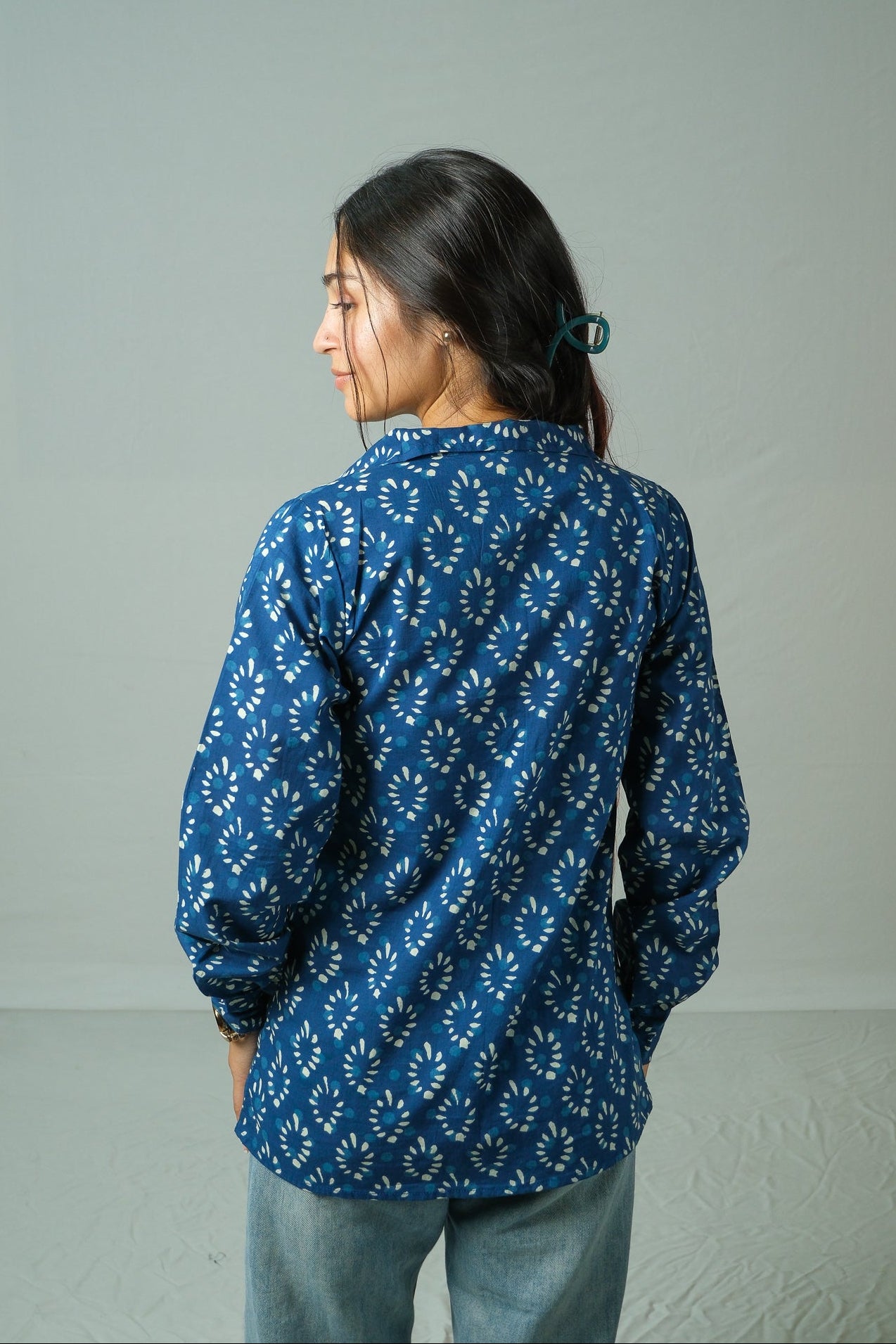 Person wearing a blue patterned shirt against a plain background